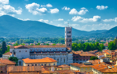 Aerial top panoramic view of Duomo di San Martino San Martin cathedral bell tower in historical centre medieval town Lucca with terracotta tiled roofs and mountain range background, Tuscany, Italy - obrazy, fototapety, plakaty