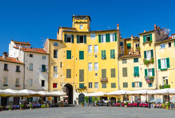 Fototapeta na wymiar Piazza dell Anfiteatro square in circus yard of medieval town Lucca historical centre, old colorful buildings with shutter windows and blue clear sky background, Tuscany, Italy