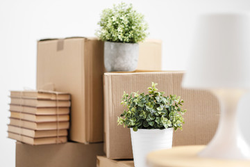 Cardboard boxes with things are stacked on the floor against the background of a white wall close up. Books and table lamps and green plants in pots. The concept of moving to a new home.