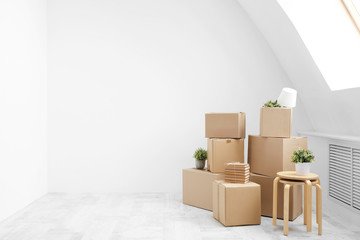 Moving to a new home. Belongings in cardboard boxes, books and green plants in pots stand on the gray floor against the background of a white wall.