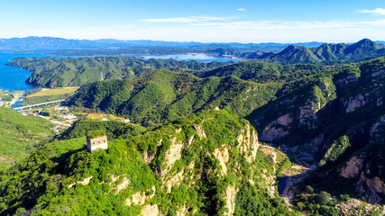 Aerial view of mountain with water reservoir  on the background. Mountain peak with beautiful blue sky and green forest. Landscape of mountain in natural reserve park. Miyun, Beijing, China.