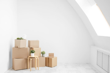 Moving to a new home. Belongings in cardboard boxes, books and green plants in pots stand on the gray floor against the background of a white wall.