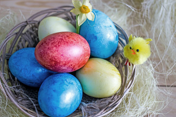 Easter card with Easter eggs of blue yellow and red in a wicker basket decorated with decorative yellow clinging. Congratulatory background with symbols of Easter