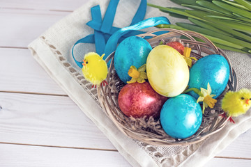 Easter card with Easter eggs of blue yellow and red in a wicker basket decorated with decorative yellow clinging. Congratulatory background with symbols of Easter