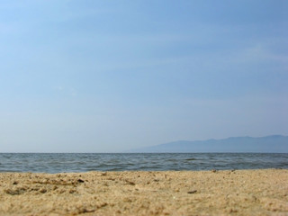 Fototapeta na wymiar Nobody on the sandy beach, clear sky. Sea background. Low the horizon, silhouette of the mountains.