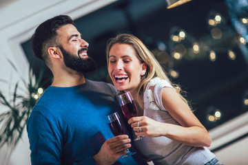 Beautiful happy young couple spending romantic evening together at home, drinking red wine, toasting