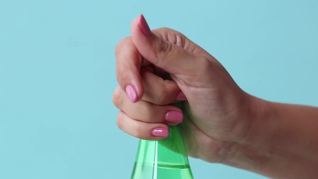 Close up view of female hand hardly opening green bottle with fresh mineral soda water isolated on blue background. Real time full hd video footage.