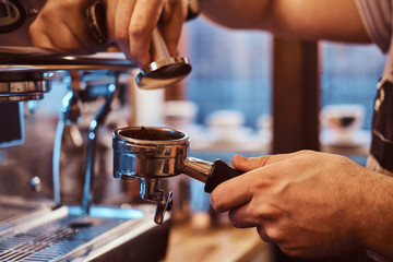 Close-up photo of a barista hand holding a portafilter with a black ground coffee in a cafe shop or...