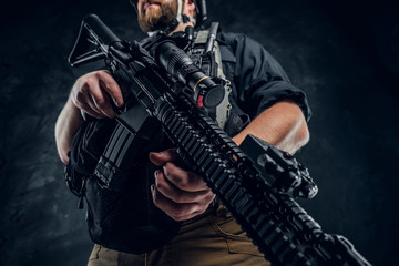 Fototapeta na wymiar A modern assault rifle in the hands of a soldier special Forces. Close-up and low angle. Studio photo against a dark textured wall