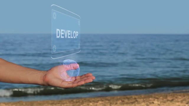 Male hands on the beach hold a conceptual hologram with the text Develop. A man with a holographic technology on the background of the sea