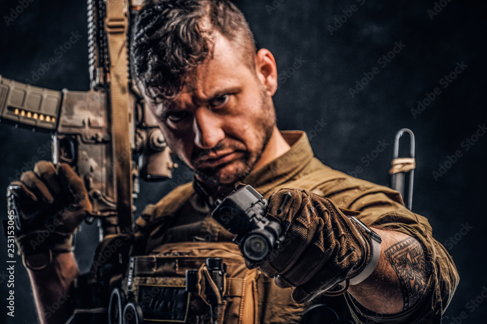 Wall mural special forces soldier wearing body armor holding assault rifle and aiming a gun at the camera. stud