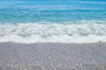 Pebble beach with azure sea water texture background.Clear sea water at a pebbly beach, pure water on the stone shore.coastline with stoned shore.gorgeous seascape.vacations to the summer paradise.