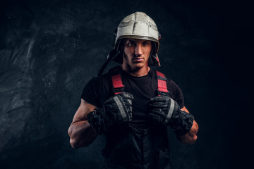 Studio portrait of a handsome man wearing a fire helmet and gloves, looking at a camera