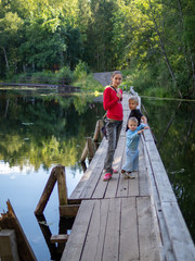 A girl with two children are standing on the old wooden bridge across a quiet river