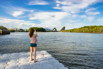 Woman tourist takes photo of Khao Khanab Nam mountains on smartphone on river  in Krabi town in Thailand