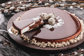 Easter cake with mirror glaze chocolate, coconut, spring flowers, quail eggs on rustic background. Happy Easter celebration. Top view, flat lay
