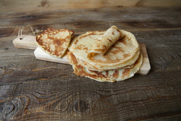 pancakes of different shapes on a board on a rustic wooden table with space for text. Shrovetide, carnival concept.