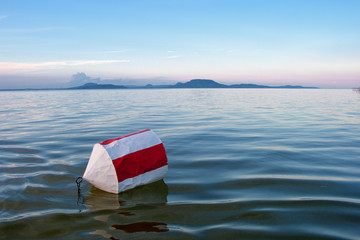 Buoy with red and white stripes on the blue water of Lake Balaton with the Badacsony mountan in the...