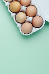 Chicken eggs in cardboard box over green background. Eggs - top view