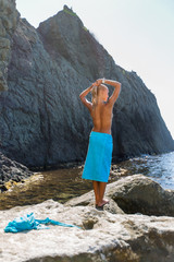 Tanned blond haired female person resting at secluded place of wild rocky seashore
