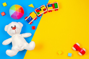 Baby kids toys background. White teddy bear, wooden train, toy car, colorful blocks on blue and yellow background