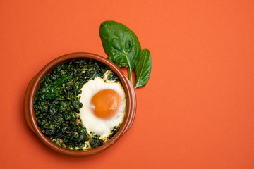 Baked spinach and egg in a clay pot. Flat lay image