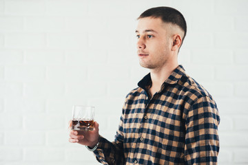 Young businessman with a glass of whiskey and a white brick wall