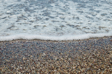 SEA TIDE ON THE PEBBLE BEACH AT SUN LIGHT, BEAUTY OF NATURE, SMALL STONES WITH WATER WAVE IN SUN LIGHT.pebble stones on the sea beach, the rolling waves.Summer vacation concept