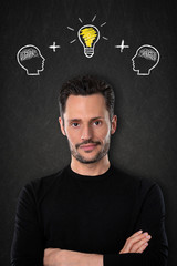 Junger Mann mit verschränkten Armen, Köpfen mit Gehirnen und Glühlbirne-Idee auf einem Tafelhintergrund.