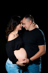 Handsome pregnant couple woman and man an posing on dark black background. Family love and expectation of the baby