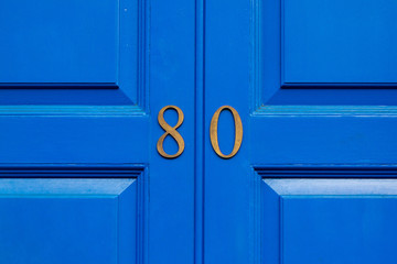 House number 80 in bronze numerals on a blue painted wooden door