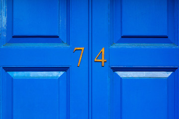 House number 74 in bronze numerals on a blue painted wooden door