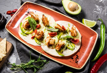 Mexican taco dish with shrimps, bell peppers, tomatoes and chili peppers on a concrete gray background