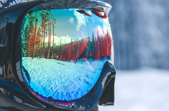 Close up picture of glasses for skiing. Snowy mountains and forest landscape view reflected in ski glasses. Sport activity in winter season. Travel concept with man. Frozen day and  snowy hills. 