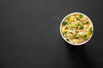 Overhead view, tasty instant noodles with beef flavoring in a cup over black surface. Flat lay, from above, overhead. Copy space.