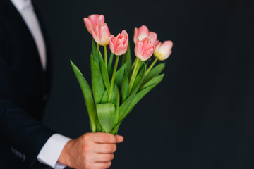 bouquet of pink tulips in men's hands in a blue suit
