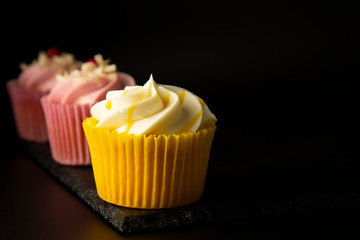 Pink and yellow cupcakes against a black background, birthday or party cupcakes. Party sweet food, desserts. Copy space.