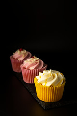 Pink and yellow cupcakes against a black background, birthday or party cupcakes. Party sweet food, desserts. Copy space.