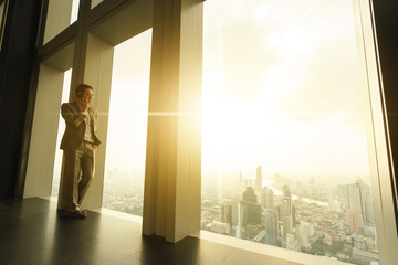Fototapeta premium Business man talk via smartphone stand by glass window in tall building with background of city