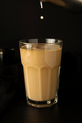 Iced coffee being poured in a tall glass with ice. Pouring milk in glass of coffee. Cold, refreshing, caffeine milkshake. Summmer drink. Black background.