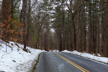 Obraz premium Acton, United States, February 27, 2019. Forest road with double yellow line in winter time, Massachusetts, United States