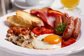Full English or Irish breakfast with sausages, bacon, eggs, tomatoes, mushrooms and beans. Nutritious and healthy morning meal.