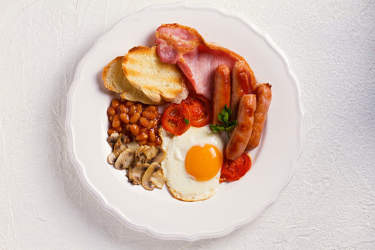 Full English or Irish breakfast with sausages, bacon, eggs, tomatoes, mushrooms and beans. Nutritious and healthy morning meal. View from above, top studio shot