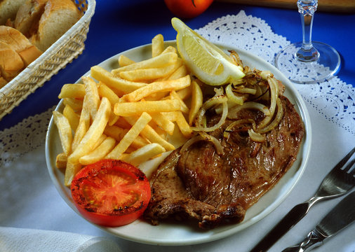 Plato con un bistec a la plancha, cebolla, tomate y patatas fritas.