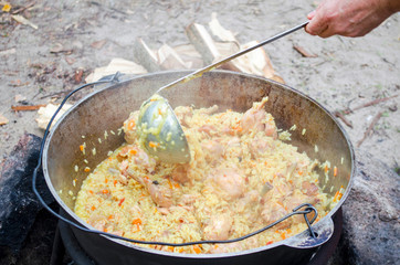 Cooking tasty pilaf in nature. Cooking pilaf in big cauldron on fire at picnic. Cooking pilaf in a...