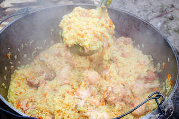 Cooking tasty pilaf in nature. Cooking pilaf in big cauldron on fire at picnic. Cooking pilaf in a...