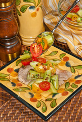 Top, front view of of an artisan plate of veal scallopini with a spoon of cut cherry tomatoes, sliced celery, and parsley with vinegar and oil dressing
