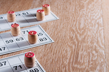 Board game lotto. Wooden lotto barrels and three game cards for a game in lotto. Wooden background. Group entertainment, family leisure. Vintage game. Excitement and good luck. Background is blurred.