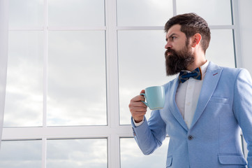 modern businessman. thoughtful bearded man drink coffee. businessman in modern formal outfit. modern life. business man at window. future success. morning inspiration. copy space. modern office