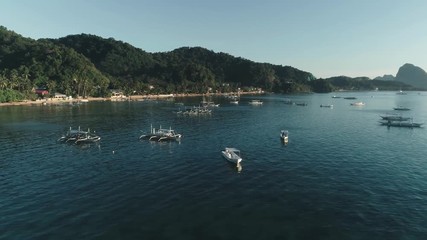 Aerial drone view of boats anchored in the bay with clear and turquoise water on the sunset. Boat and yacht in the tropical lagoon. Tropical landscape. El Nido, Palawan island, Philippines.
